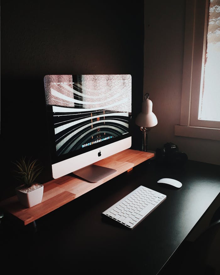 Sleek modern home office with a desktop computer, keyboard, lamp, and potted plant.